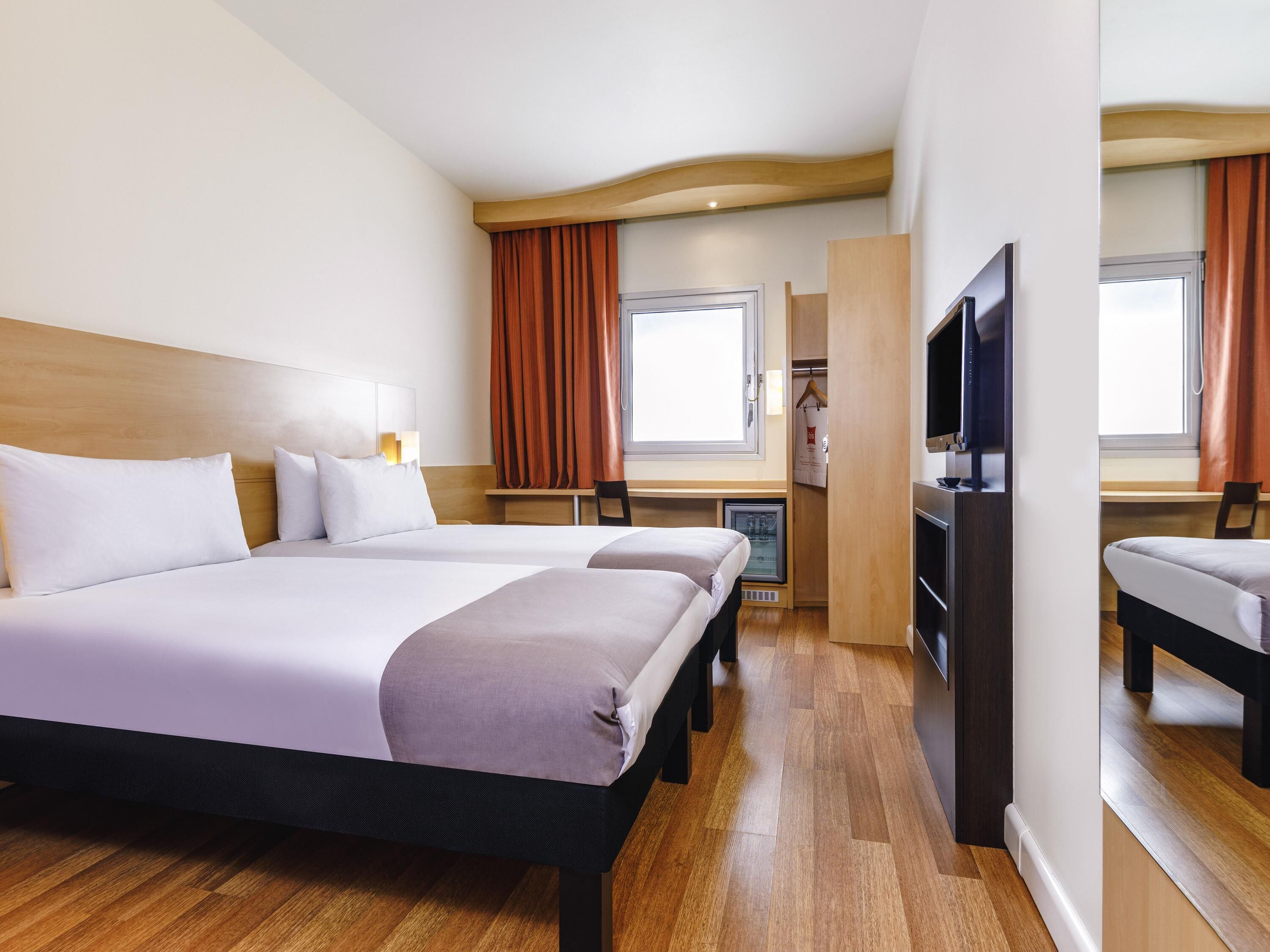 A hotel room with two beds, a desk, a television, and a wardrobe.