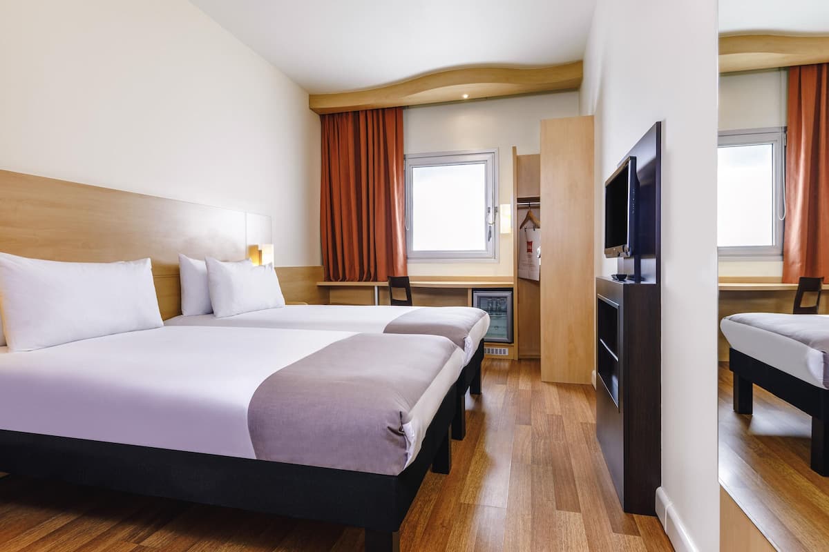 A hotel room with two beds, a desk, a television, and a wardrobe.