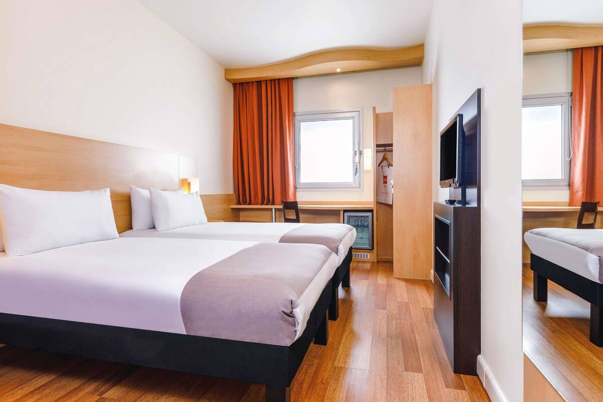 A hotel room with two beds, a desk, a TV, and a wardrobe.