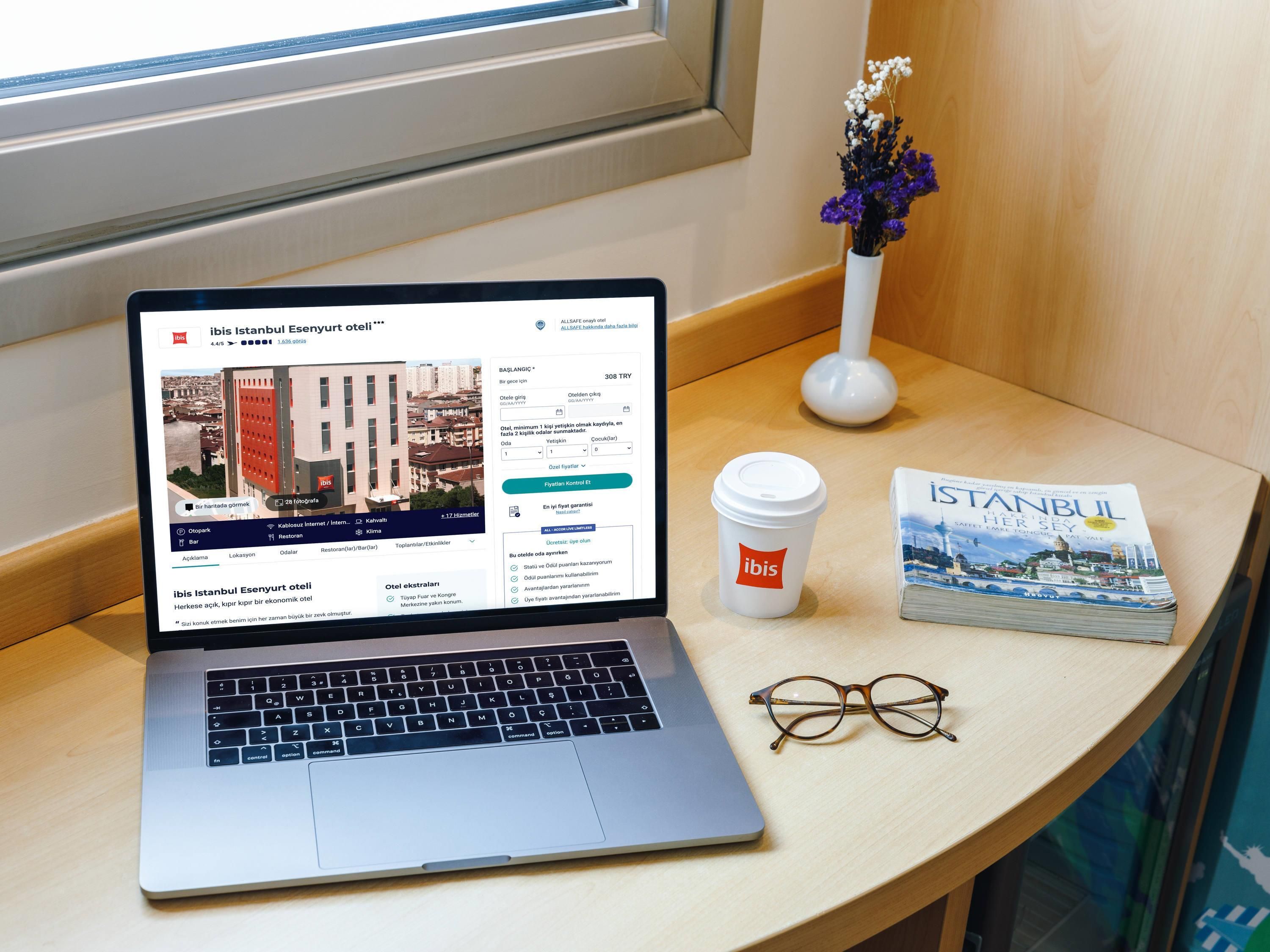 Una laptop sobre una mesa, con un libro y una taza de café a su lado.