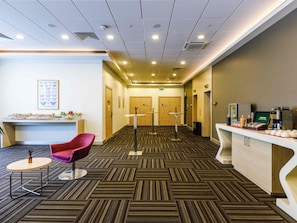A hotel lobby with a reception desk, a coffee station, a seating area with a red chair, and a patterned carpet. - ibis Istanbul Esenyurt (Istanbul)