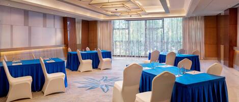 A conference room with multiple tables and chairs, large windows with curtains, and a patterned carpet.