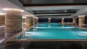 Een binnenzwembad met marmeren zuilen, helderblauw water en een modern plafond.