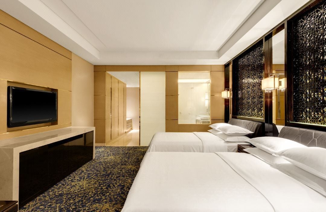 Een hotelkamer met twee bedden, een flatscreen televisie, een bureau en een decoratief wandpaneel.