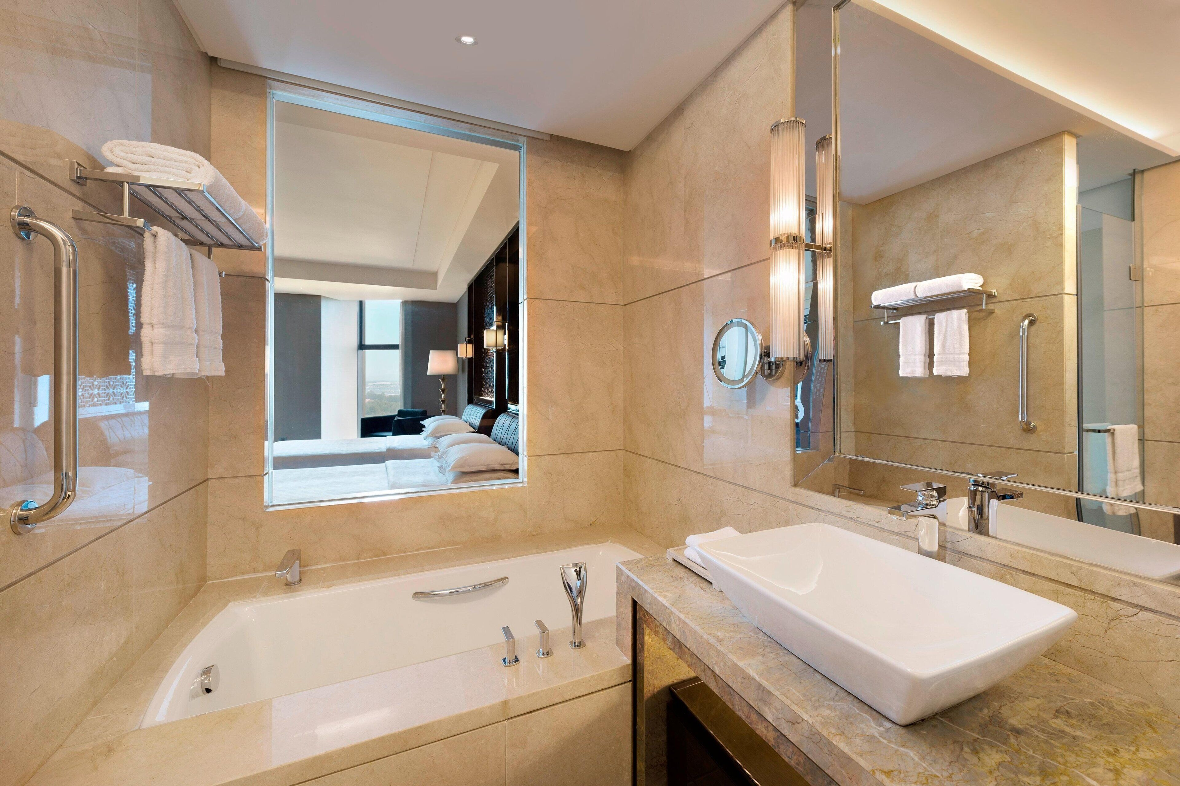 A modern bathroom with a large bathtub, a rectangular sink, and a large mirror. There are towels on a rack and a glass shower enclosure.