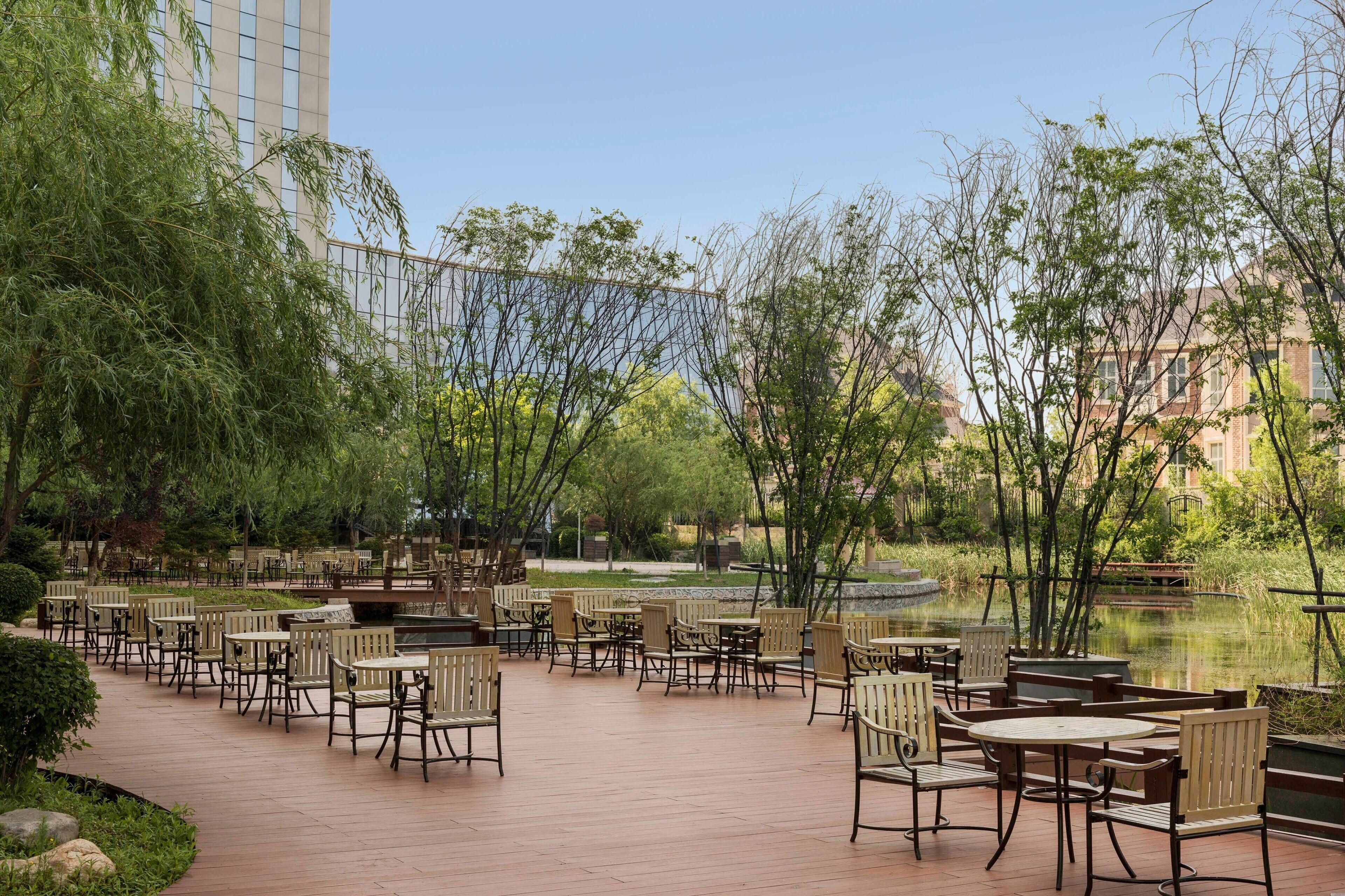 Un espace extérieur aménagé avec des tables et des chaises, entouré de verdure et bordé d’un étang.