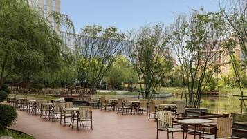 Un espace extérieur aménagé avec des tables et des chaises, entouré de verdure et bordé d’un étang.