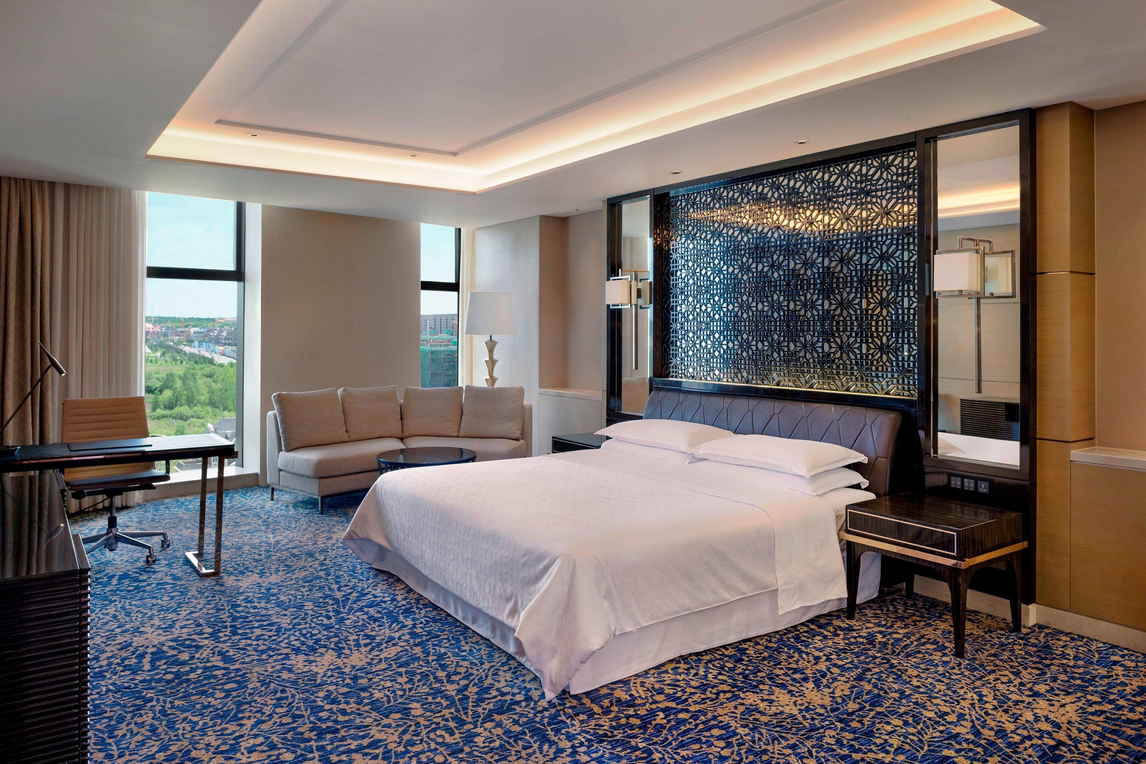 A hotel room with a large bed, a sofa, a desk, and a view of the city.