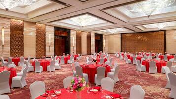 A banquet hall with round tables set for dining, white chairs, and red tablecloths.