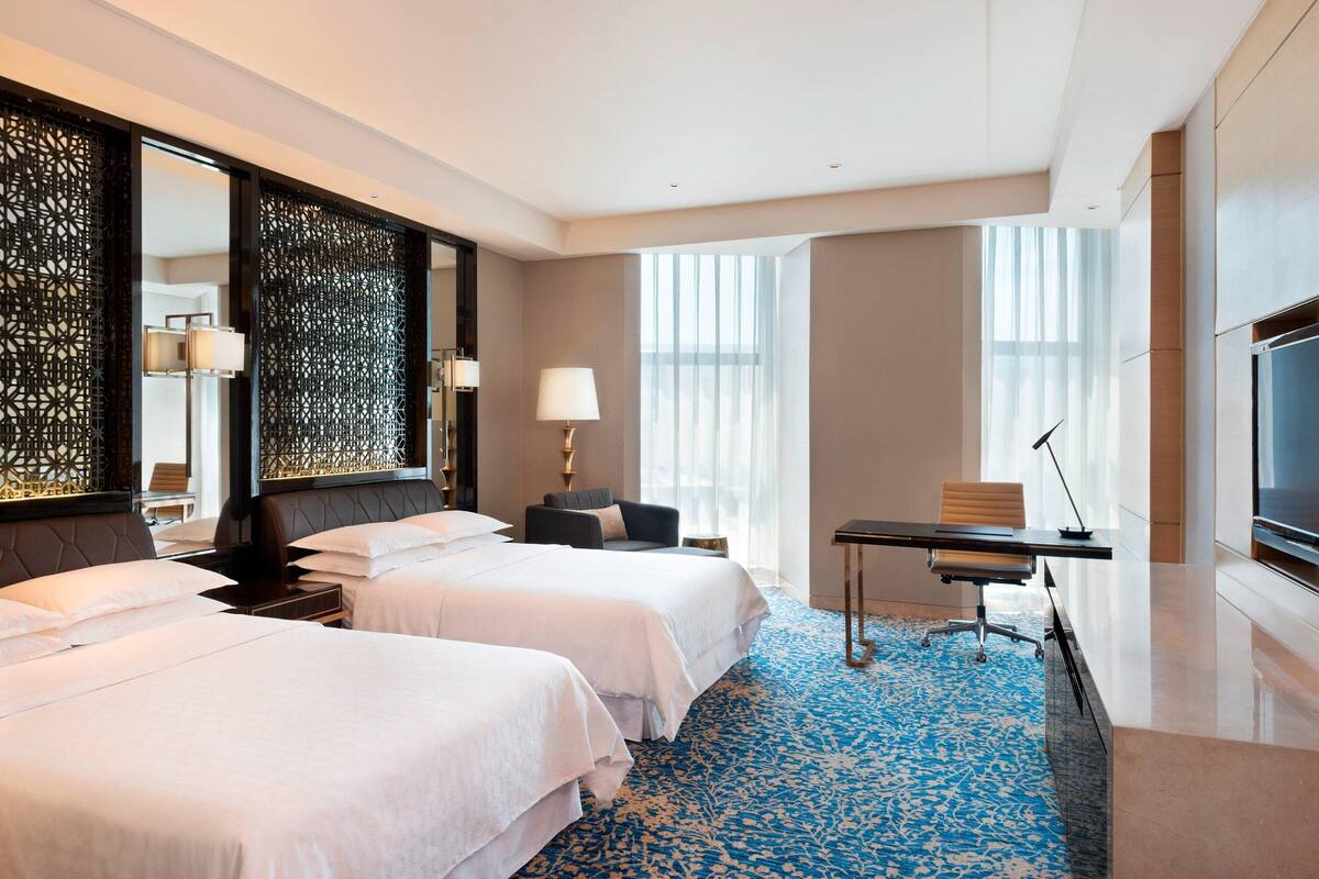 Een hotelkamer met twee bedden, een bureau, een televisie en grote ramen.