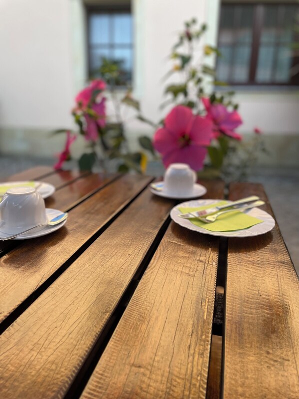 Una mesa de madera con un hervidor blanco, una taza blanca y un plato verde con una cuchara.