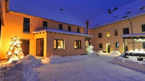A snow-covered courtyard with a building featuring multiple windows and a snow-covered roof. - Pension Marlis (Moritzburg)