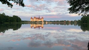 Un edificio grande e histórico con fachada simétrica y varias torres, reflejado en un lago tranquilo.