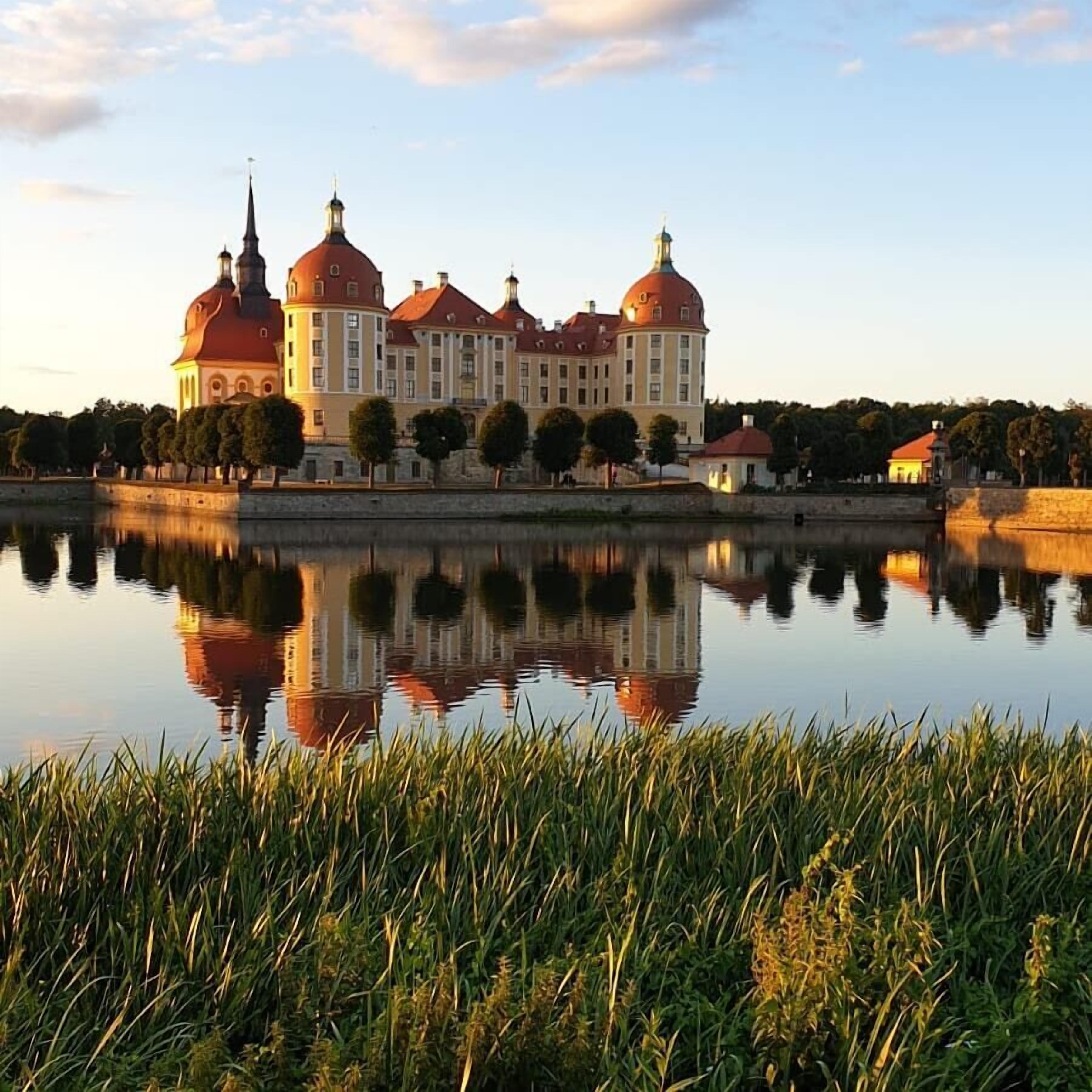 A large building with multiple domed roofs and a reflection in the water.