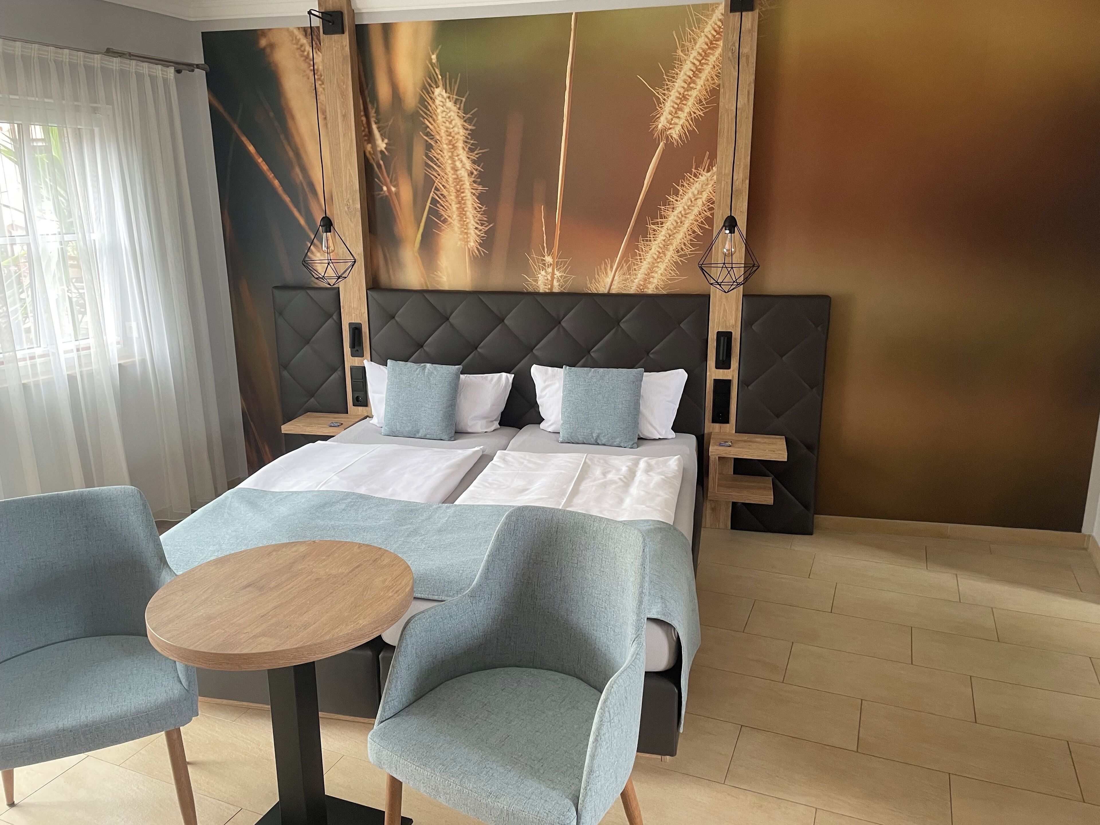 Une chambre d’hôtel moderne avec un grand lit, deux tables de chevet, une table ronde en bois et deux fauteuils bleus.
