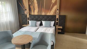 Une chambre d’hôtel moderne avec un grand lit, deux tables de chevet, une table ronde en bois et deux fauteuils bleus.