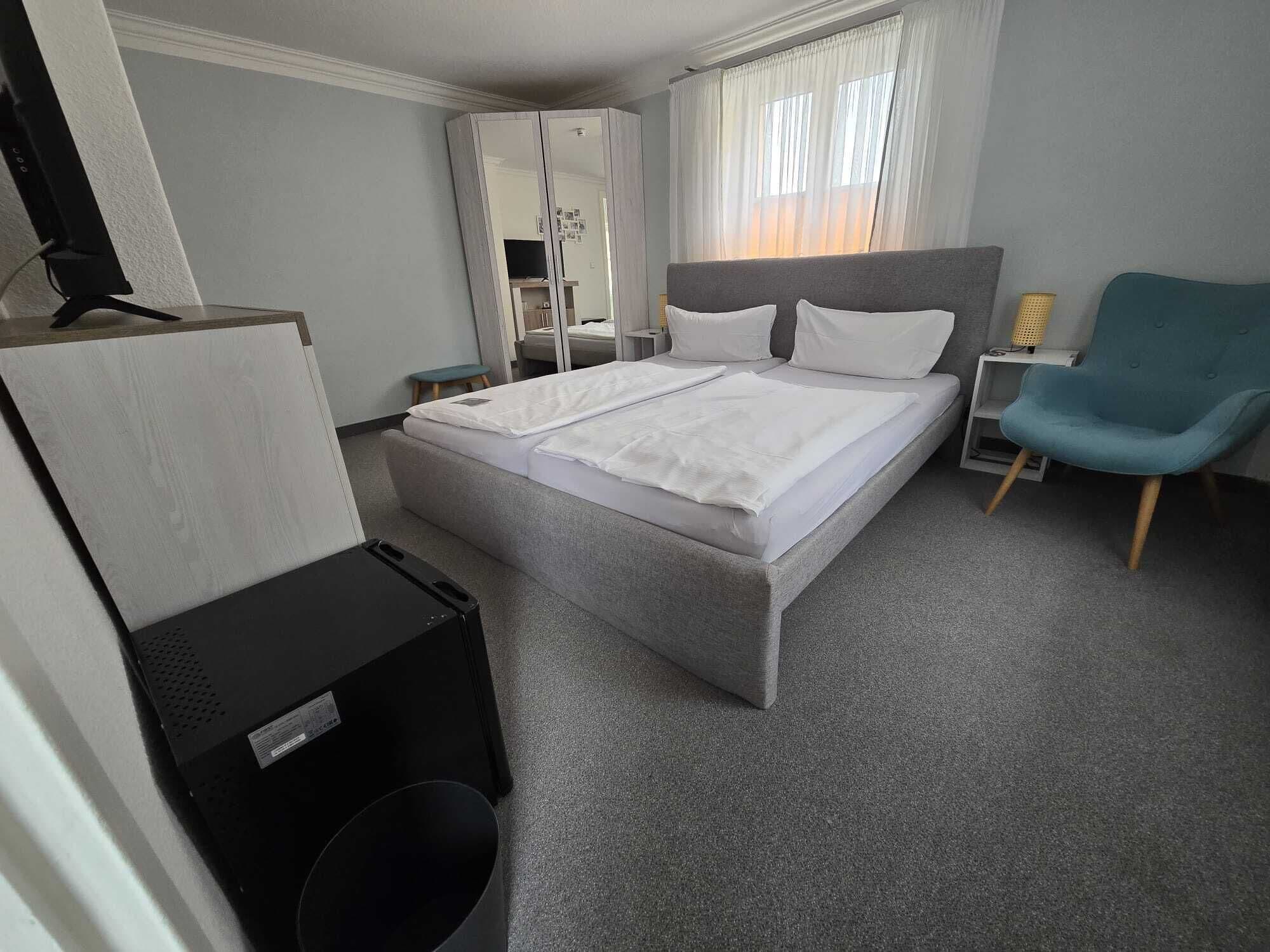 A hotel room with a bed, a desk, a chair, and a wardrobe.