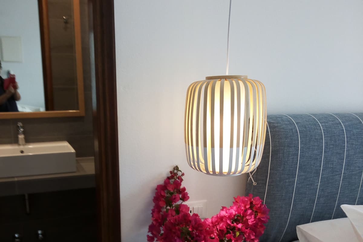 A bathroom with a mirror, sink, and a bedside table with a lamp and flowers.