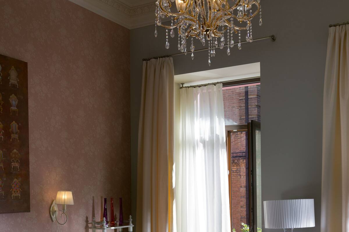 Un dormitorio con colcha morada, candelabro, estantería y vista al exterior.