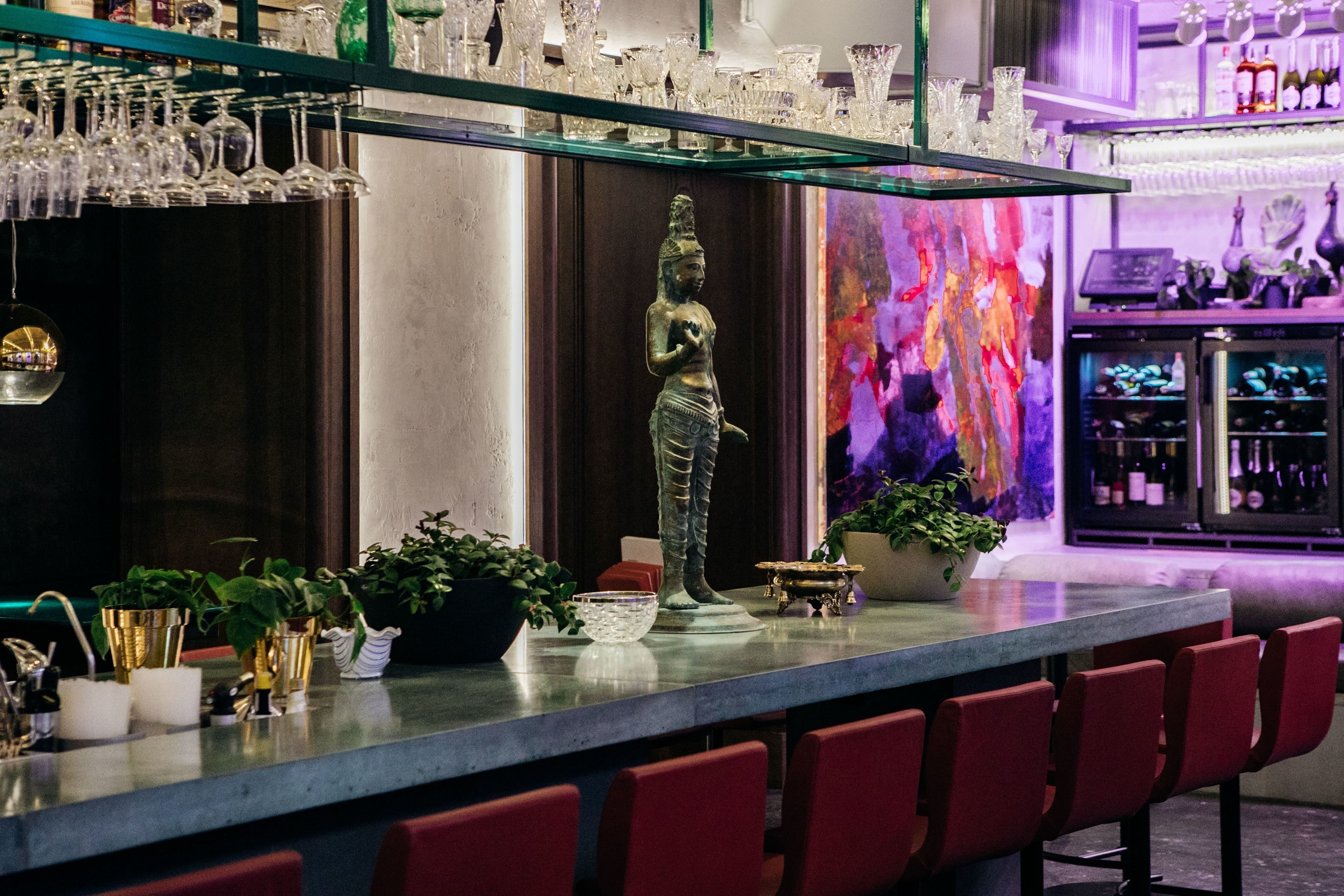 Uma área de bar com um balcão comprido, banquetas vermelhas e uma estátua.