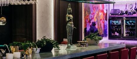 Uma área de bar com um balcão comprido, banquetas vermelhas e uma estátua.