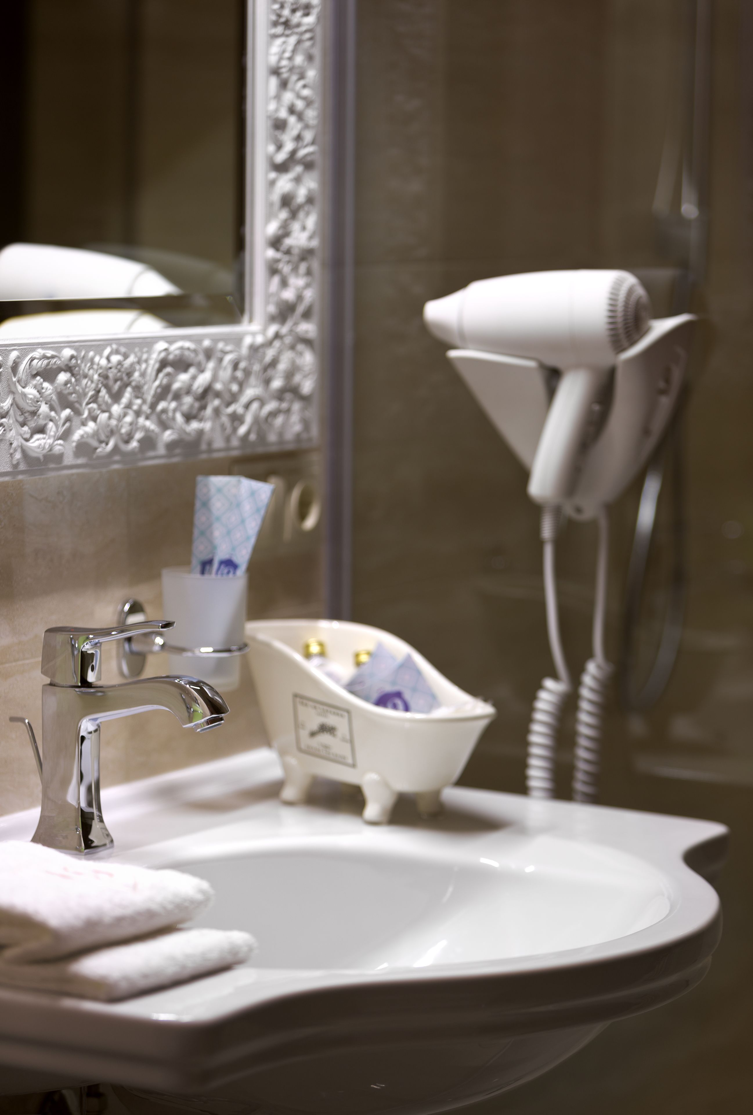A bathroom with a sink, mirror, hairdryer, and a small bathtub.