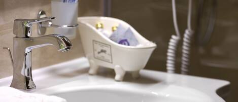 A bathroom with a sink, mirror, hairdryer, and a small bathtub.