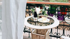 A round glass table with a bottle of wine and a cake on a balcony with wicker chairs and potted plants. - Hotel 19 (Kharkiv)