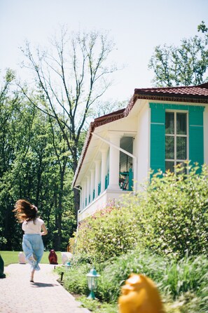 Un edificio de fachada blanca y contraventanas verde mar, rodeado de follaje.