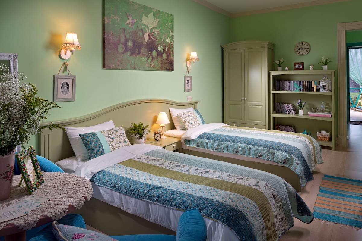 A bedroom with two beds, a bookshelf, and a large window.