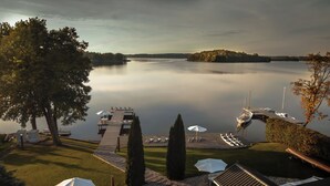 A lakeside resort with a dock, lounge chairs, umbrellas, and a boat. - Hotel Galery69 (Stawiguda)