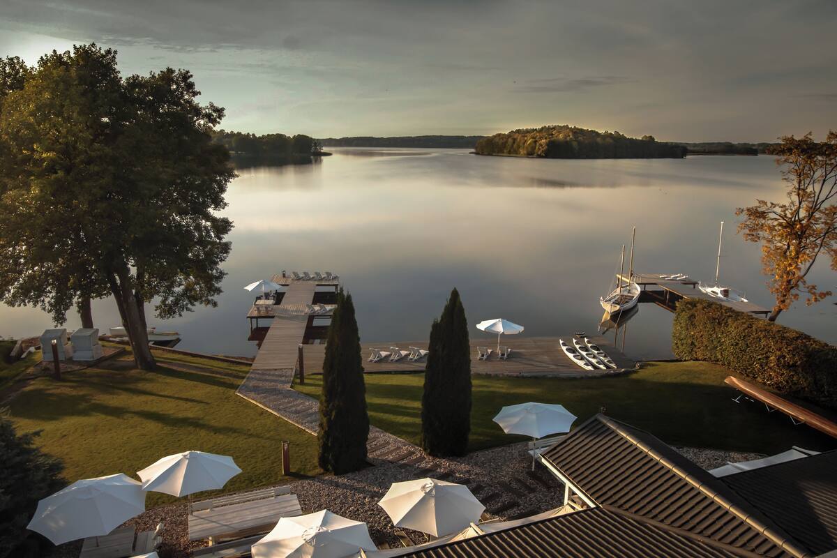 Un resort a orillas del lago con un muelle, sillas de descanso, sombrillas y un bote.