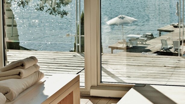 A modern room with a large glass window overlooking a wooden deck and a body of water. - Hotel Galery69 (Stawiguda)