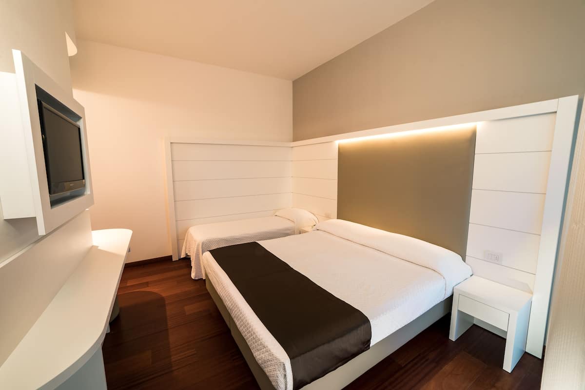 A modern hotel room with a large bed, a smaller bed, a bedside table, and a TV mounted on the wall.