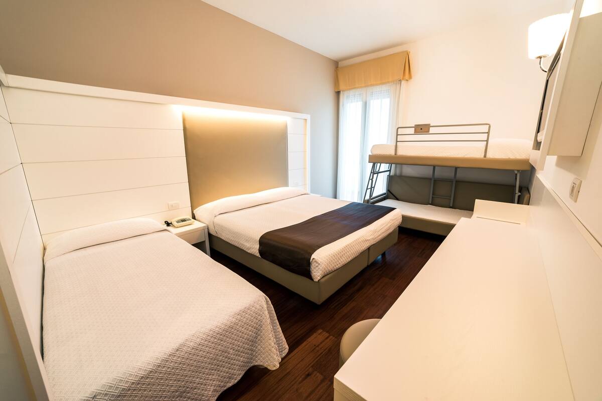 A hotel room with two beds, a desk, and a bunk bed.