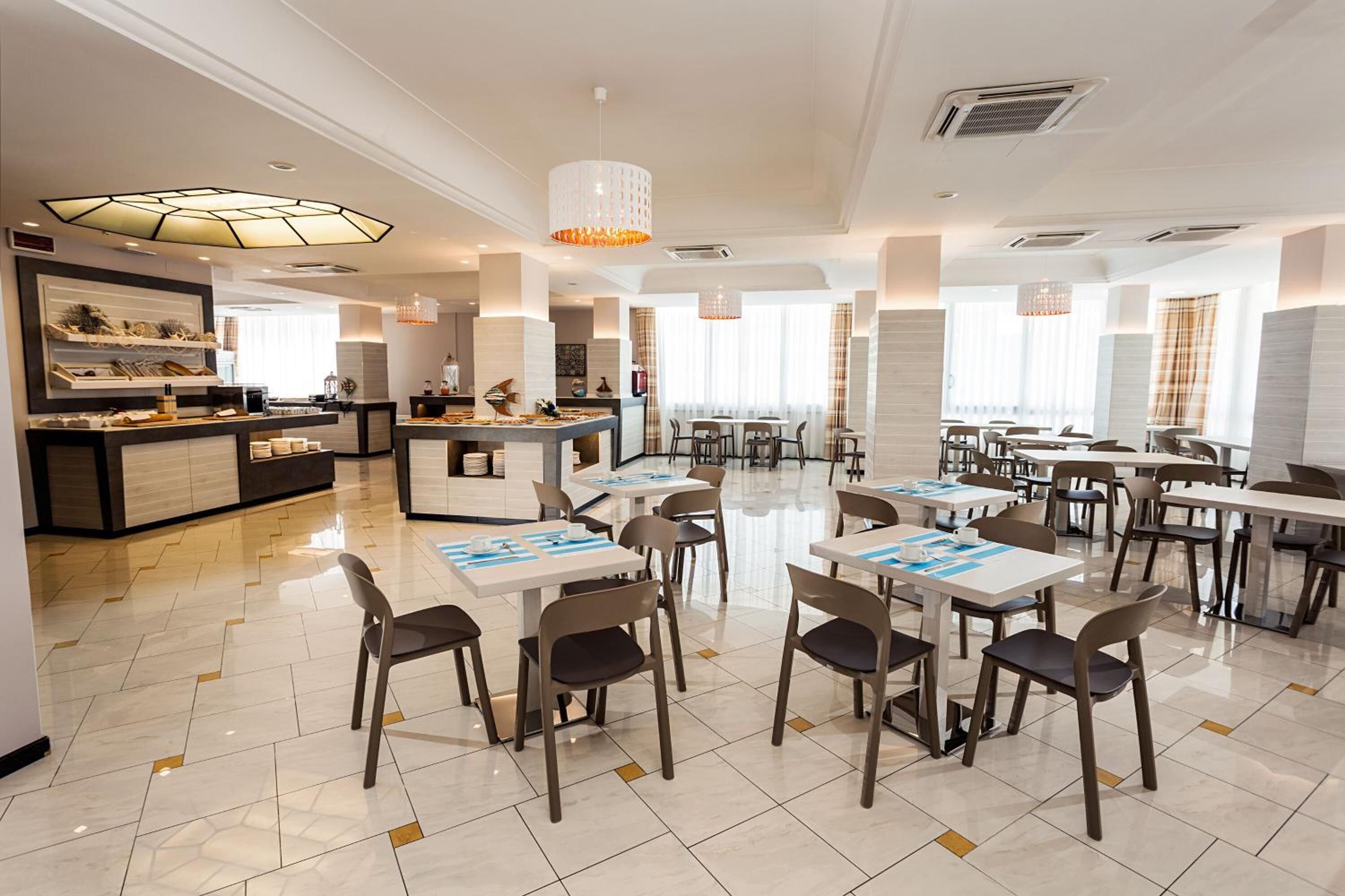 A spacious dining area with multiple tables and chairs, a central bar area, and a modern chandelier.