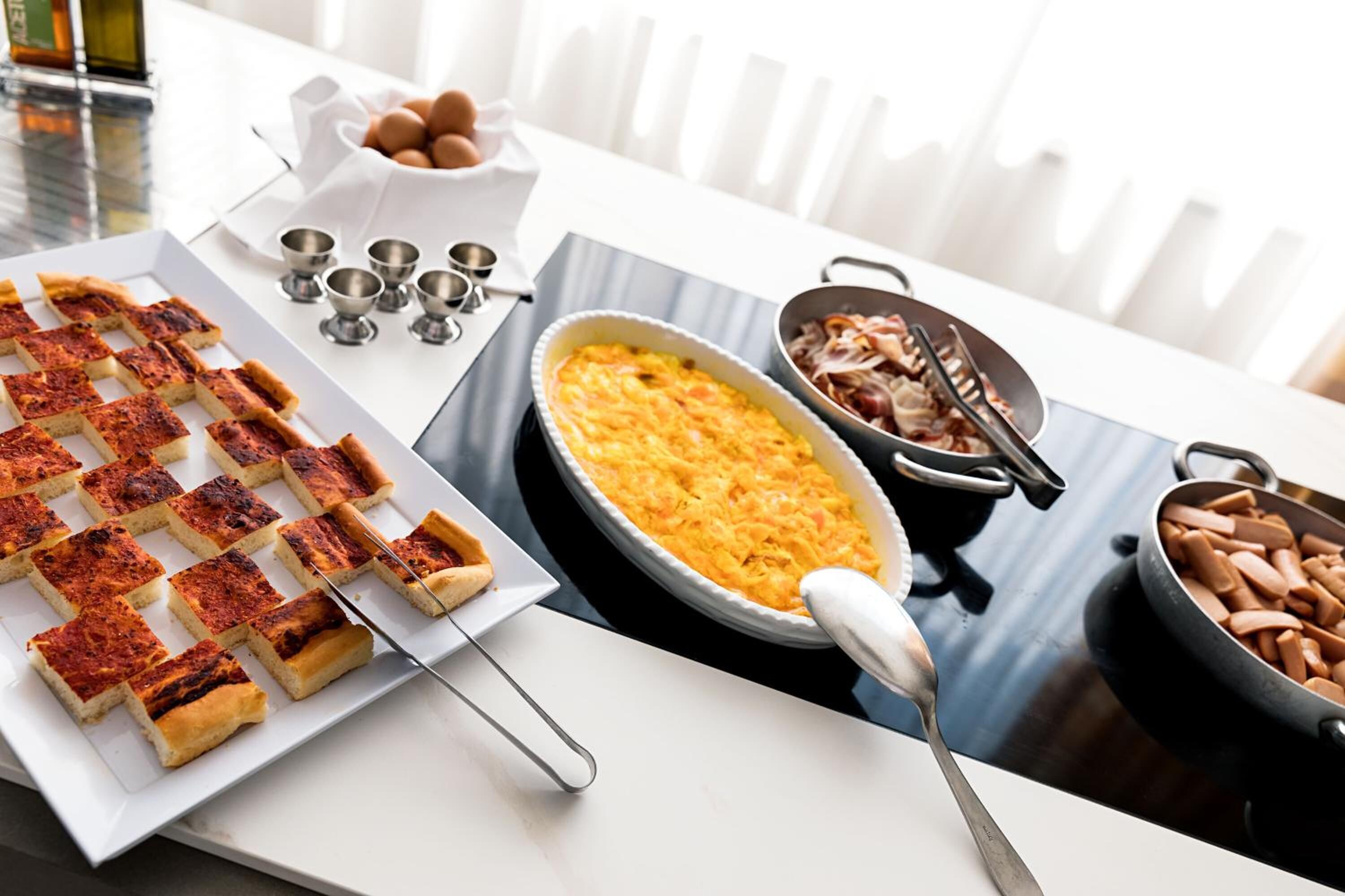 A breakfast setting with a charcuterie board, a baked dish, and a pan of sausages.
