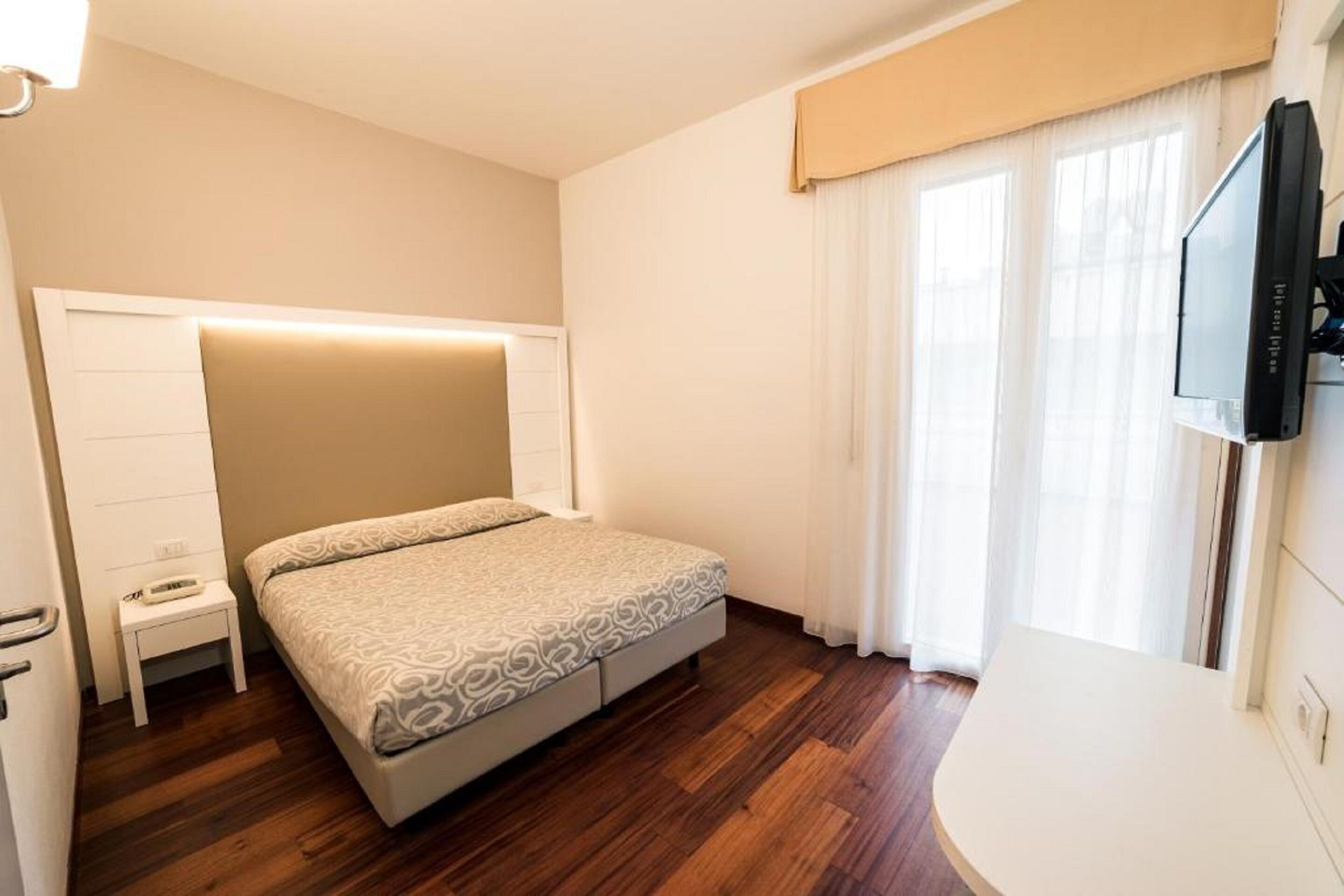 A bedroom with a bed, bedside table, and a TV mounted on the wall.