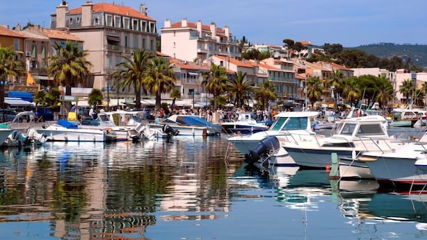 A marina with boats docked, surrounded by buildings with red-tiled roofs and palm trees. - Une Nuit à Bord Bandol (Bandol)