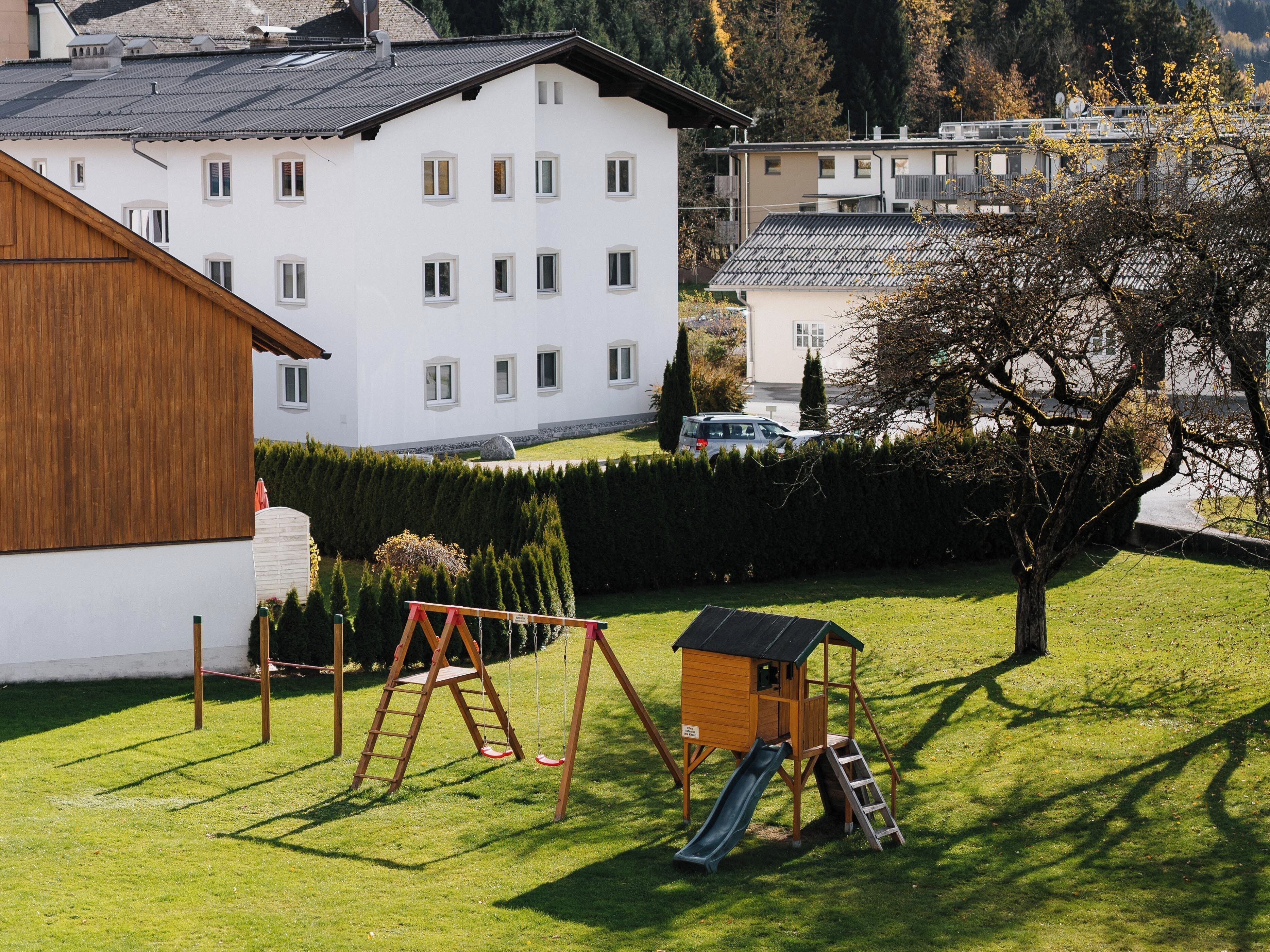 Una zona residencial con un edificio blanco, una estructura de juego de madera y una casita con un tobogán.