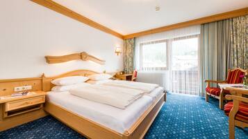 Ein Hotelzimmer mit einem hölzernen Bett, einem Nachttisch, einem Schreibtisch mit Stuhl und einem Fenster mit Vorhängen.