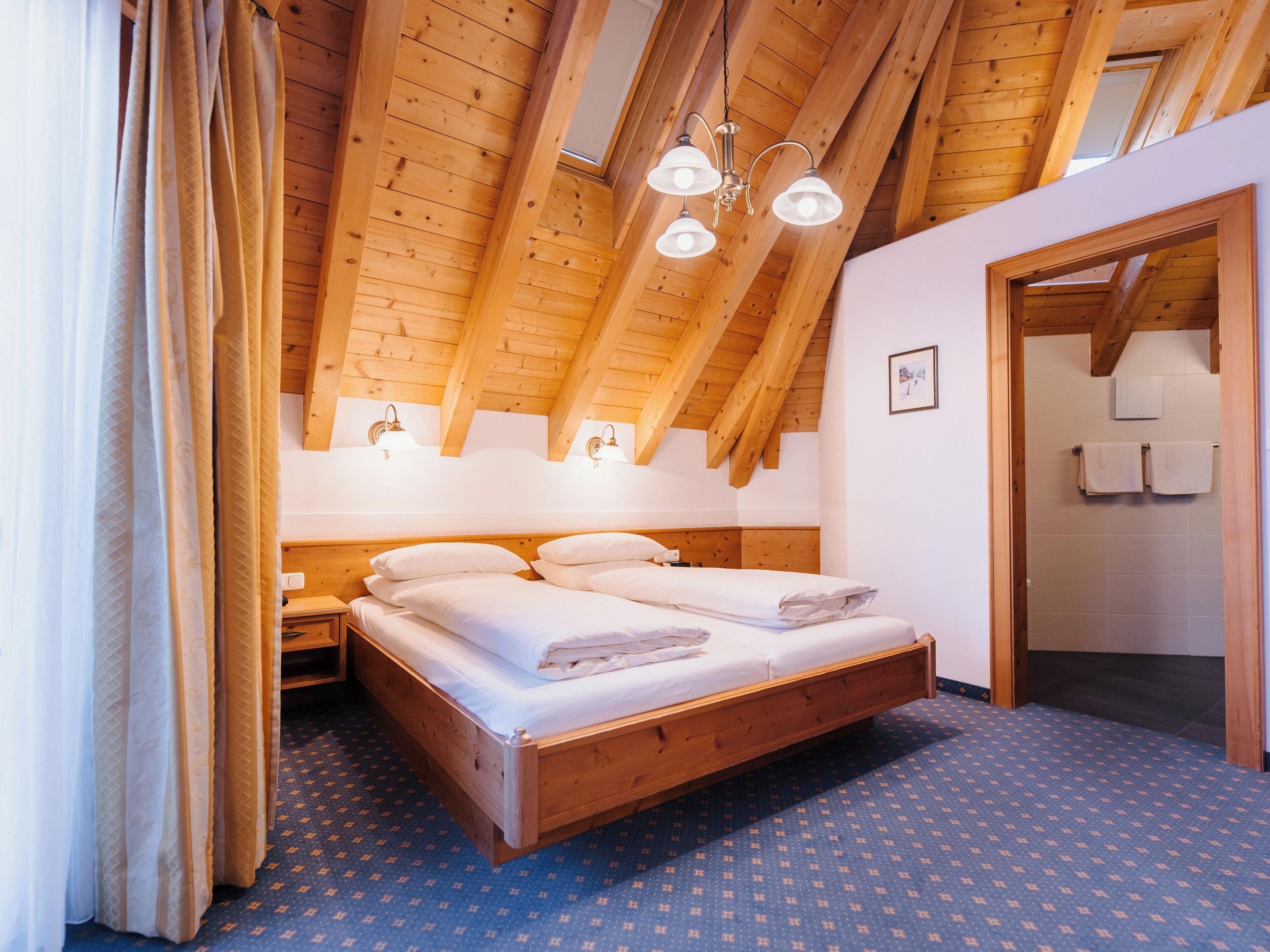 A bedroom with a wooden ceiling, a bed with white linens, and a patterned carpet.