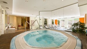 Une piscine intérieure moderne, dotée d’un jacuzzi, de chaises longues et offrant une vue sur l’extérieur.