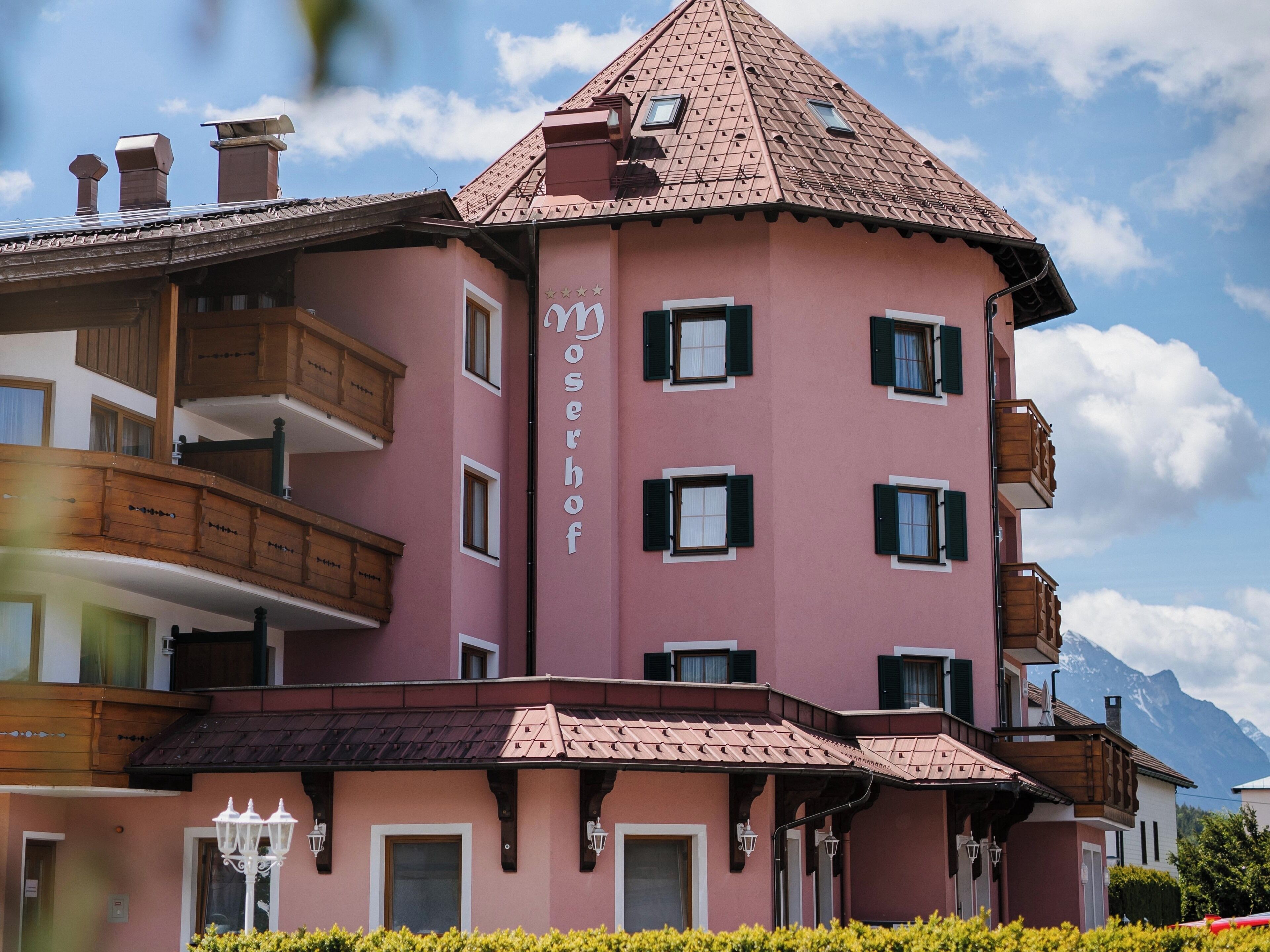 A multi-story building with a pink facade, balconies, and a peaked roof.