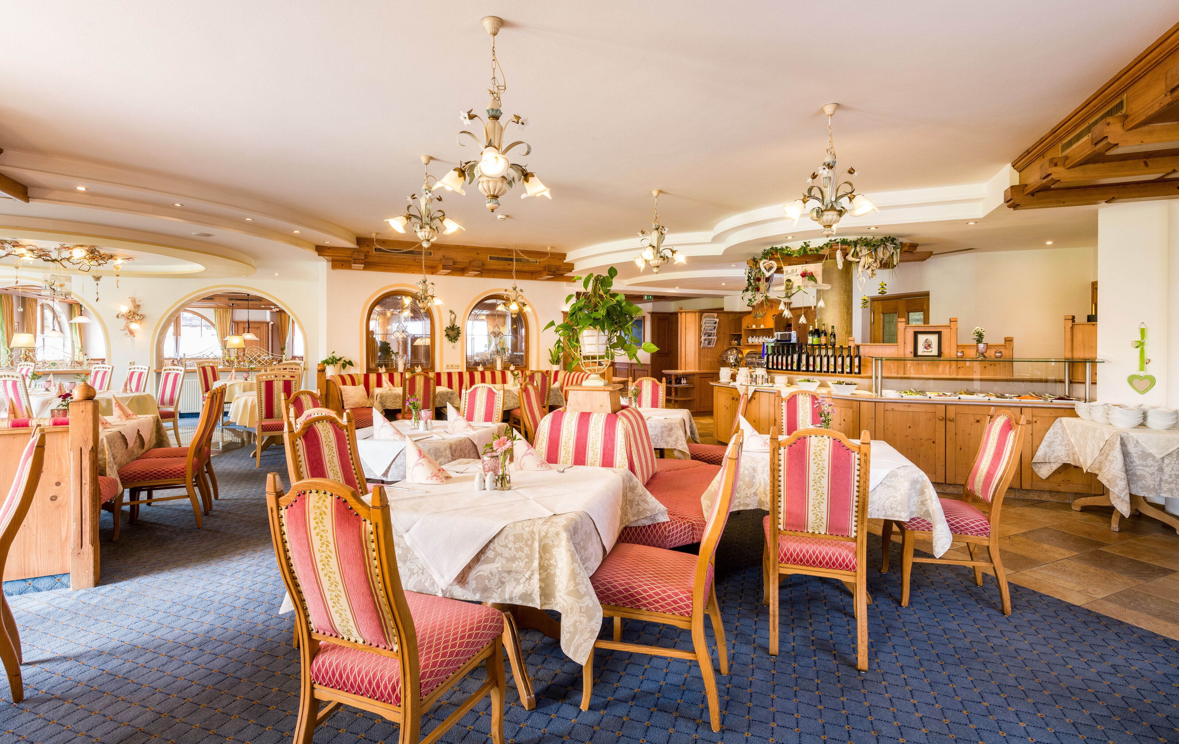A restaurant with wooden tables and chairs, chandeliers, and a bar area.