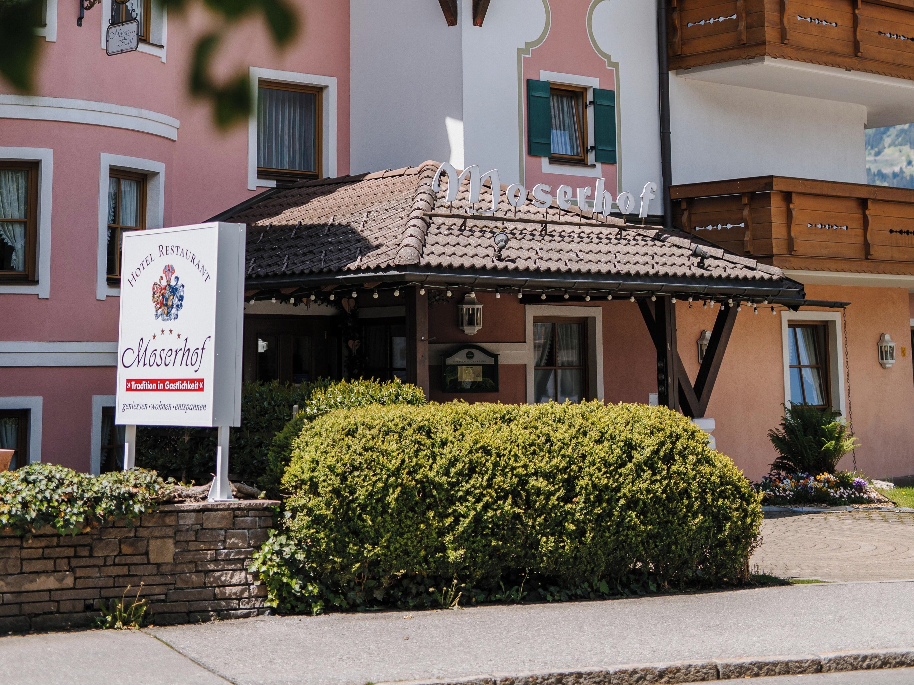Ein Restaurant des Hotels Moserhof mit traditioneller europäischer Architektur, darunter ein Ziegeldach und ein Schild mit dem Namen und dem Slogan des Hauses.