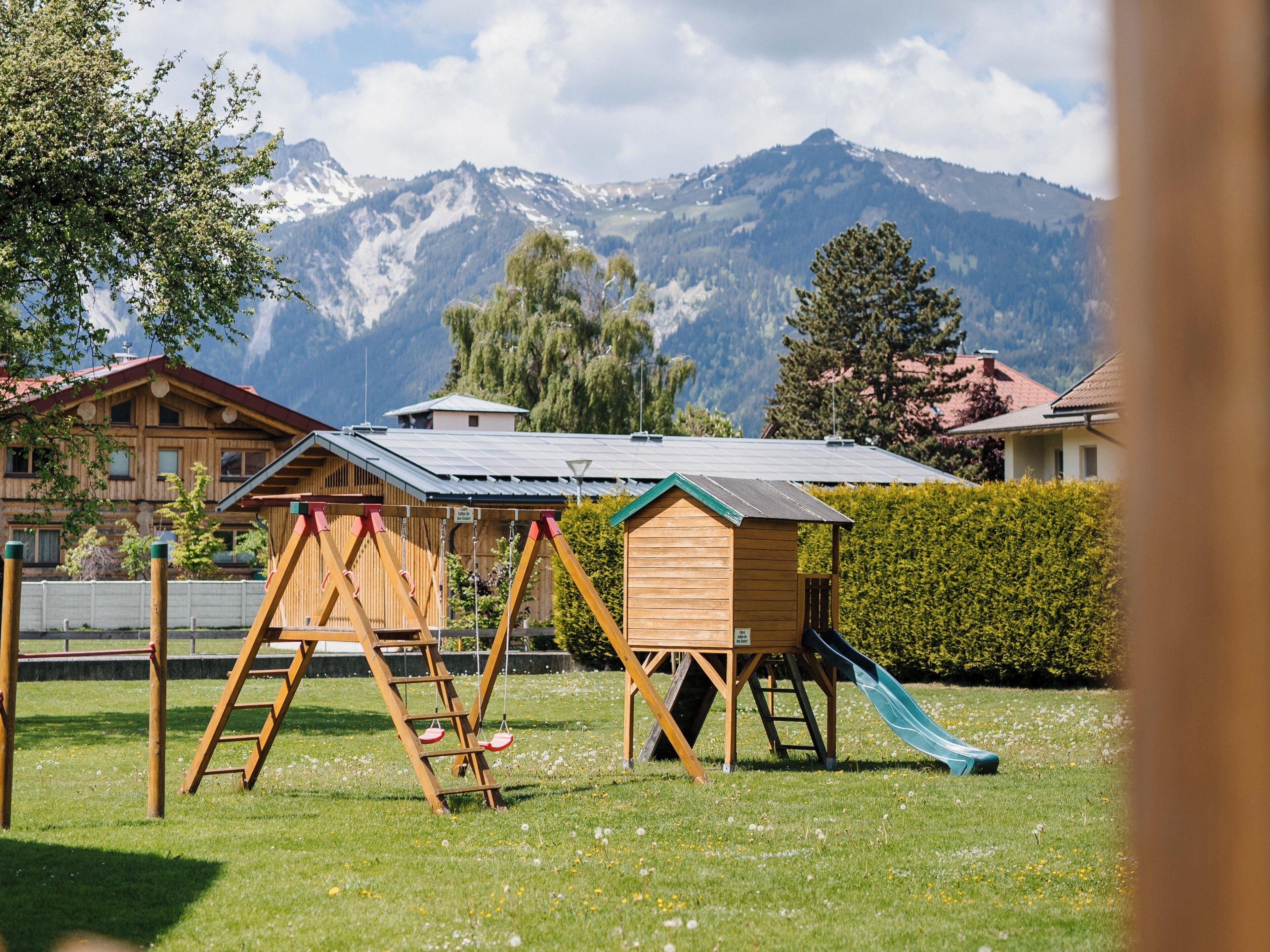 A playground with a slide and swings, set against a backdrop of mountains and houses.