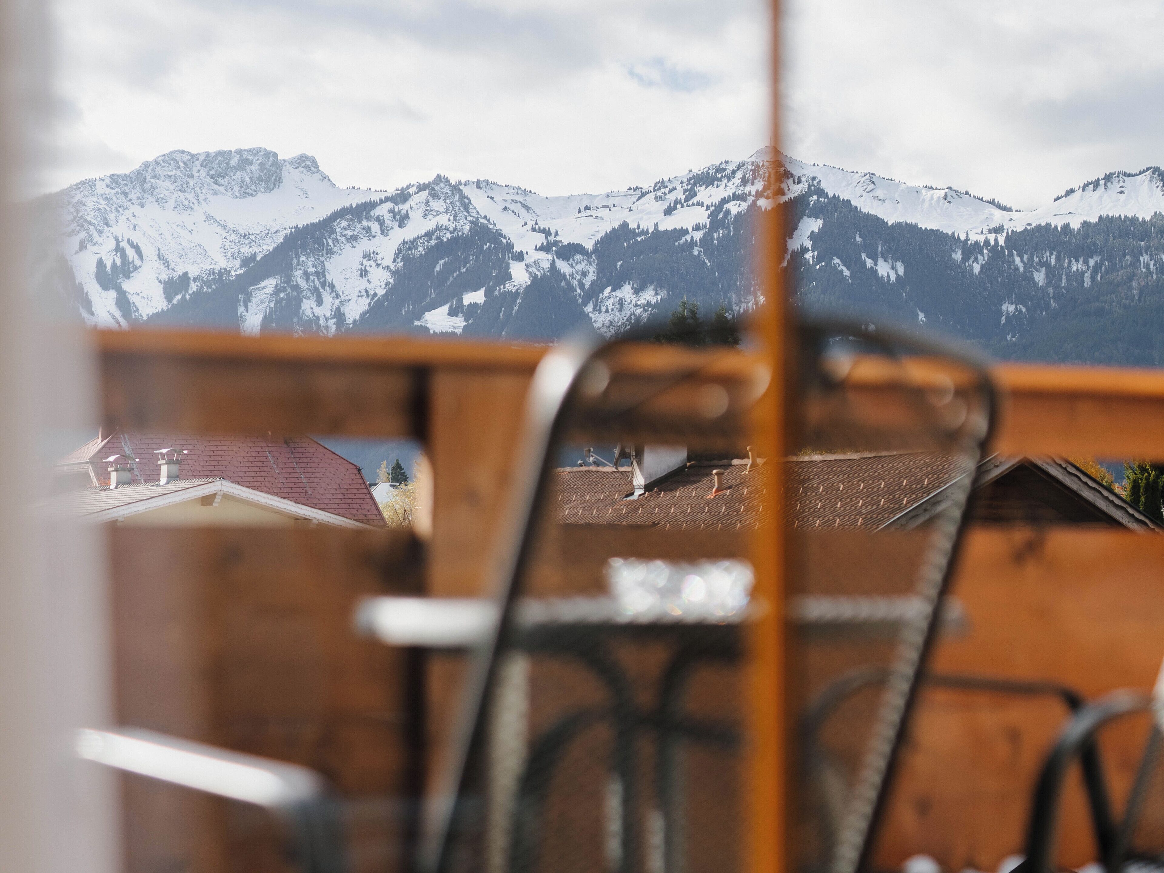 Blick auf schneebedeckte Berge durch einen Holzzaun, im Vordergrund ein Stuhl.