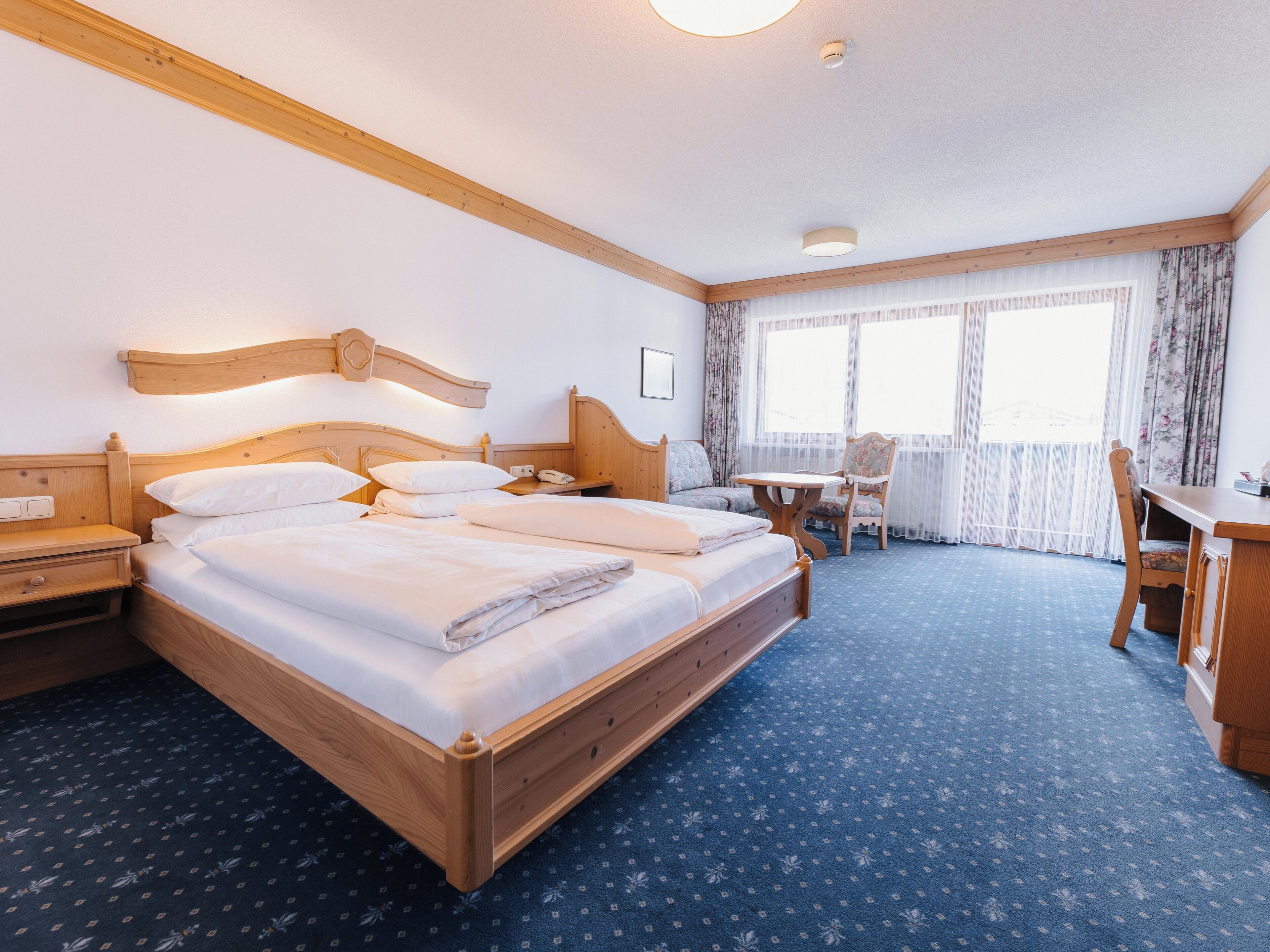 Ein Hotelzimmer mit einem großen Bett, Nachttischen, einem Schreibtisch, einem Stuhl und einem Fenster mit Vorhängen.