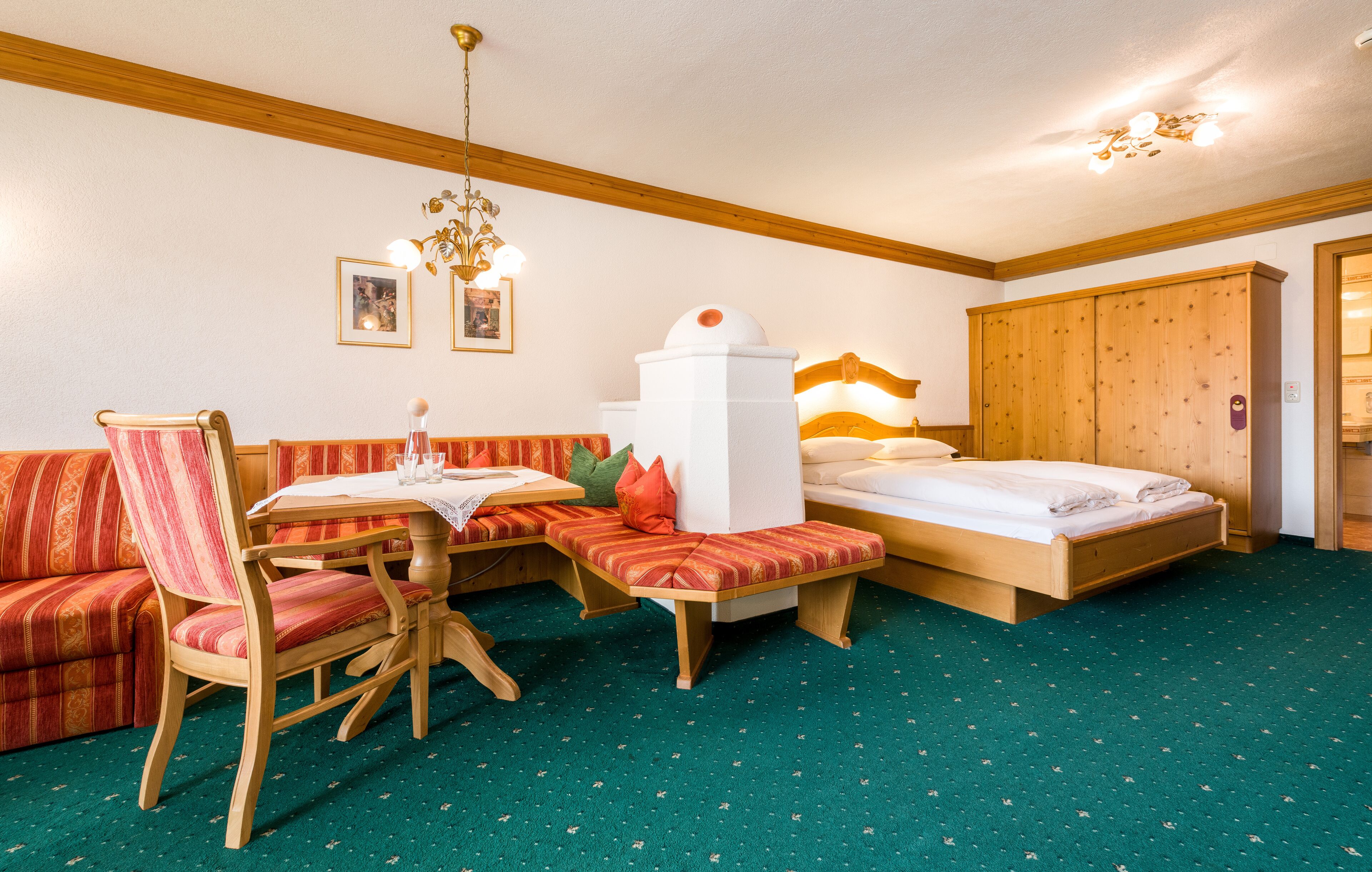 A hotel room with a wooden bed, a bench, a dining table with chairs, and a sofa.